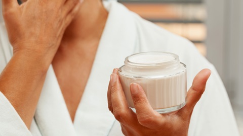 mulher de roupão branco a aplicar um creme de rosto